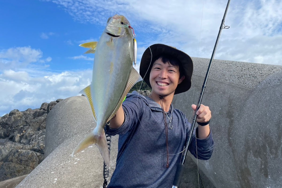 テトラポッドの上で、釣り上げた青物を手に笑顔を見せるアングラー